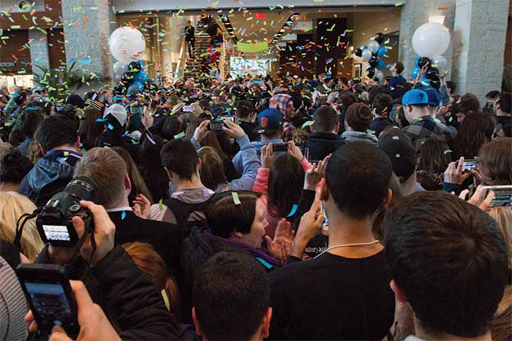 A crowd of people in the Campus Center grand hall pointing their cellphones toward the confetti fall in the sky