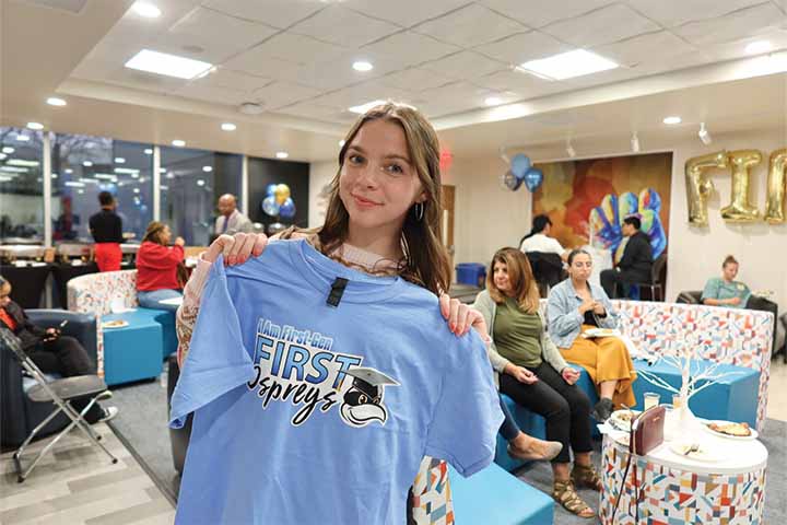 A student holds up a blue shirt reading I am First-Gen, First Ospreys