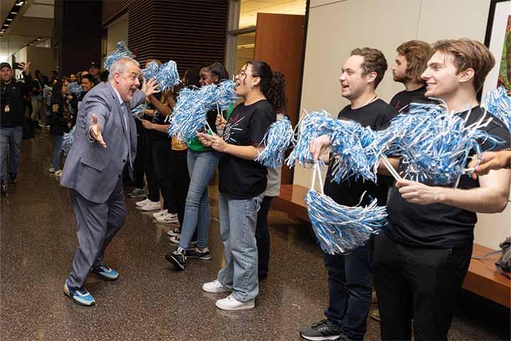 President Joe excitedly greets students holding pom-poms in the Campus Center Grand Hall