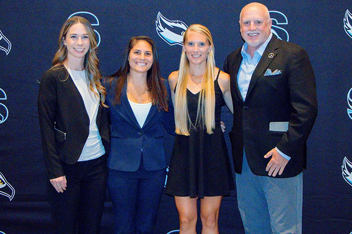Three women and one men pose in front of a Stockton athletics step-and-repeat banner