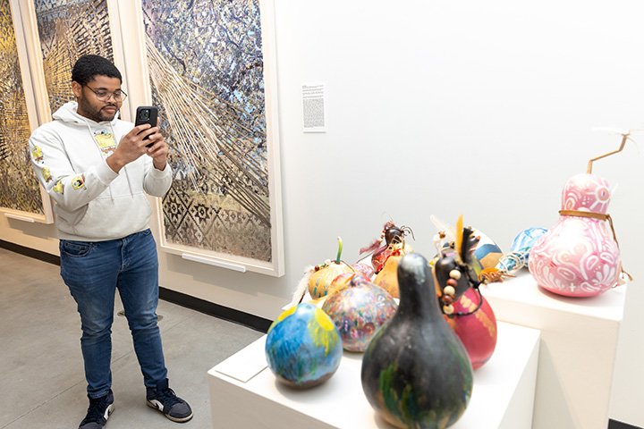A student uses his cell phone to take a picture of Indigenous gourd artwork on display in Stockton's Art Gallery
