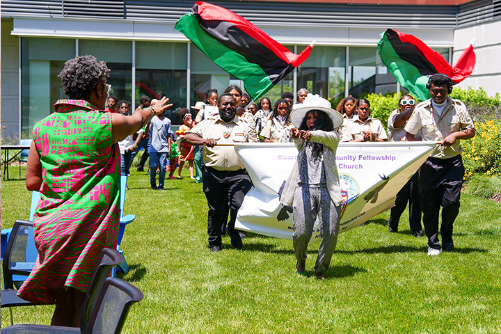 Beverly Vaughn wearing a large white hat leads a small parade of students waving the Pan African flag through the quad space at the John F. Scarpa Academic Center in Atlantic City