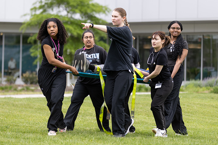 Six nursing students carry a patient on a stretcher to a safer area during an emergency preparedness drill