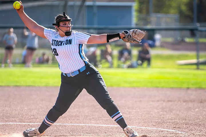 Nerina Tramp in white Stockton uniform winds up to pitch a softball
