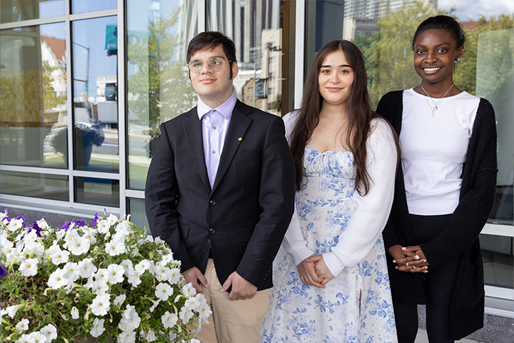 Dickson Moreno, Yaisha Rios, Channon Wilson stand outside the John F. Scarpa Academic Center at Stockton Atlantic City with a pot of white flowers in the foreground
