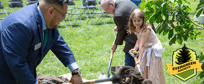 Three individuals, ranging in ages, helping plant a tree on Stockton's campus