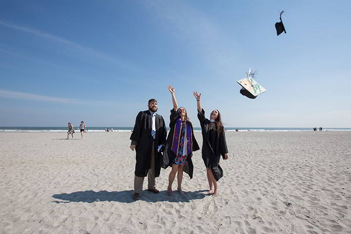 Ospreys toss their caps to the sky on the beach in a celebratory moment after Commencement in Boardwalk Hall
