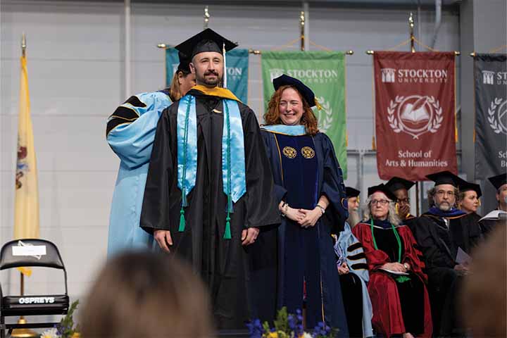 Jared Lombardi in graduation cap and gown receiving his master's hood