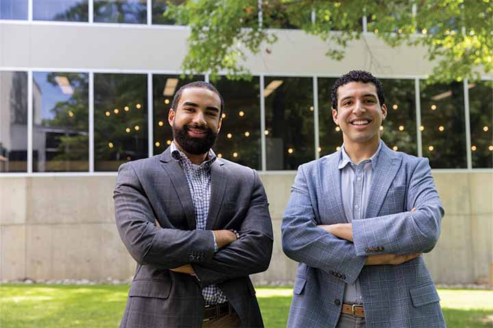 Francisco Vizcaino-Martinez and Sage Del Valle wearing business suits with arms crossed in front of Stockton's main academic spine