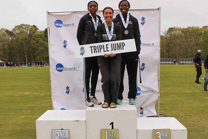 Emma Petrolia Ashanae Morrison, Khristina Washington stand on a winners' podium with their medals and holding a sign saying "Triple Jump"