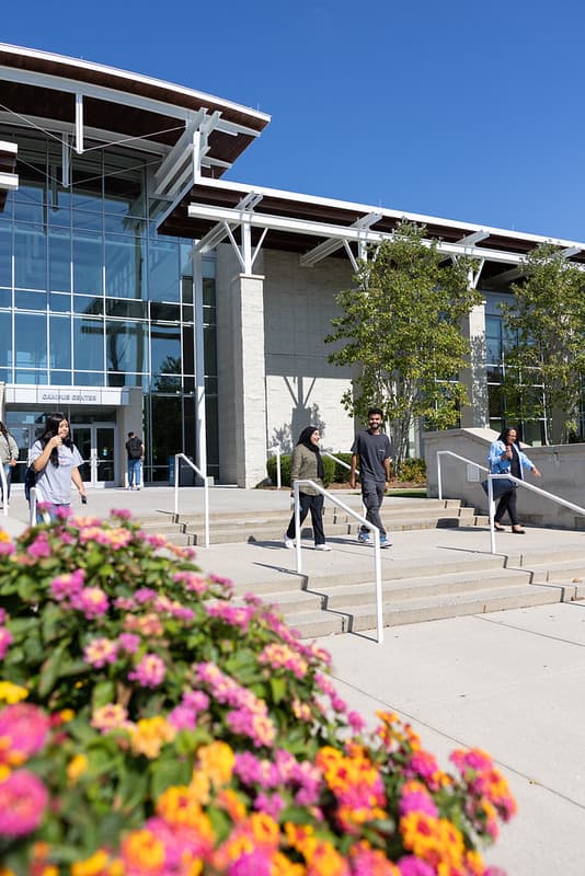 Two students walk down the front steps of the Campus Center with colorful flowers in the foreground